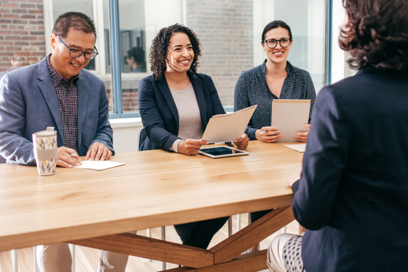 Professional interview for jobs in Vancouver with three interviewers reviewing resumes and engaging with a candidate in a bright, modern office.